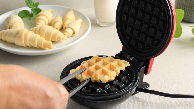 finished croffle in waffle maker with croissants on a plate