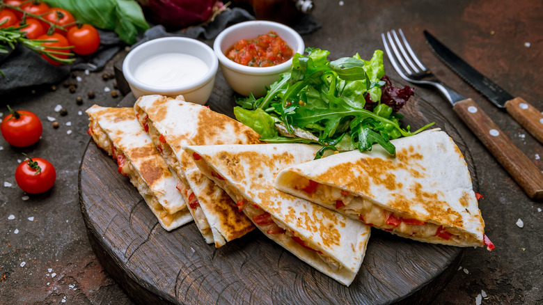 Quesadilla cut into triangles served alongside greens and containers of salsa and sour cream