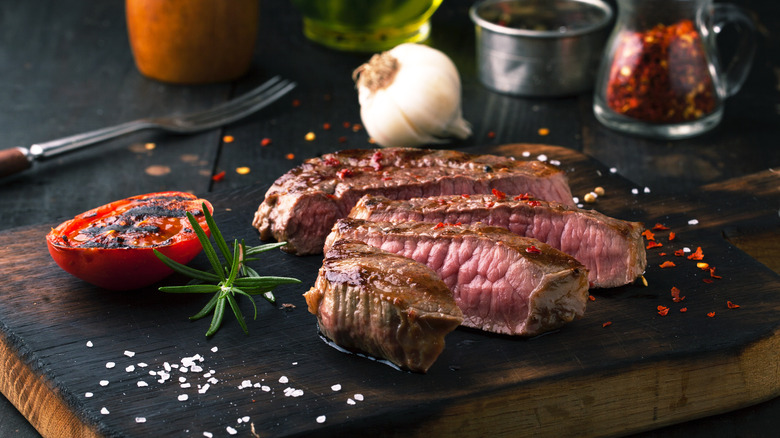 Grilled ribeye steak on cutting board with garlic, herbs, and spices