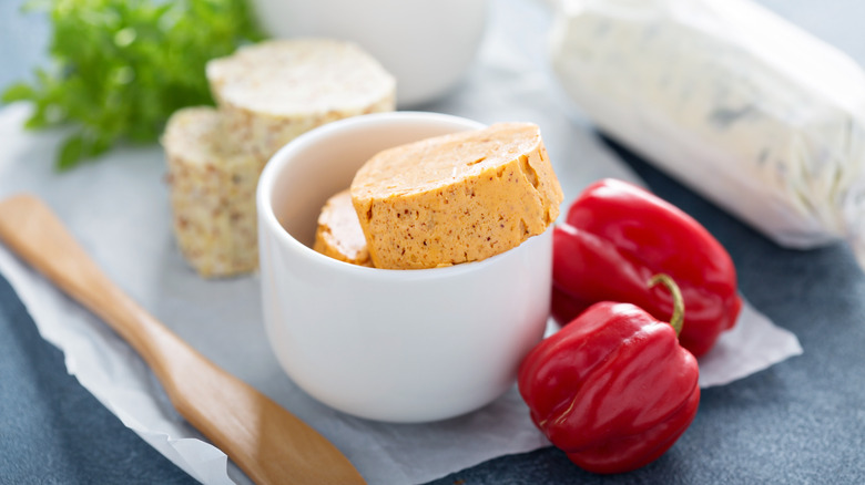 Slices of compound butter in bowl with chili and herbs