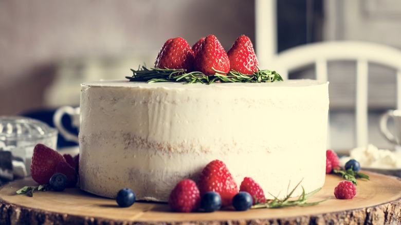 Frosted cake topped with berries on table