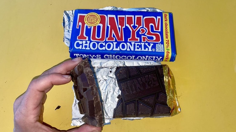 Hand holding unwrapped chunk of Tony Chocolonely 70% Dark Chocolate Bar