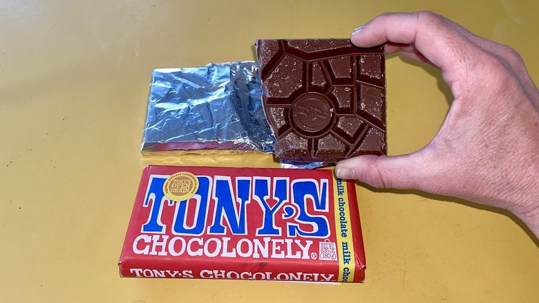 Hand holding unwrapped a chunk of Tony Chocolonely Milk Chocolate Chocolate Bar