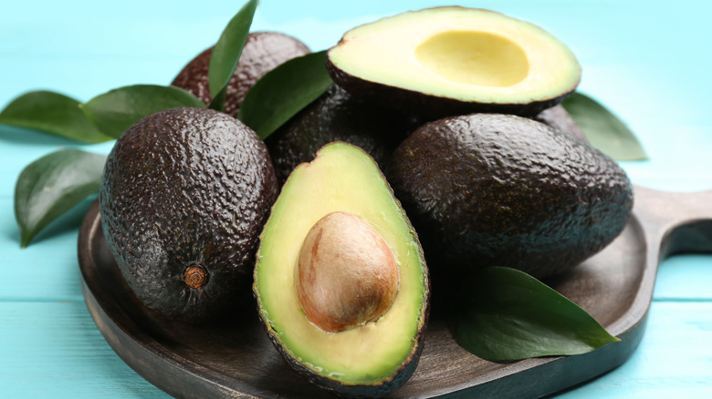 Whole and cut avocados on a round wooden board with blue background