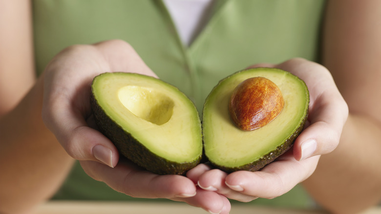 hands holding two avocado halves