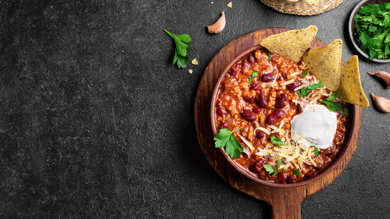 Chili in a bowl with herbs, sour cream, and tortilla chips.