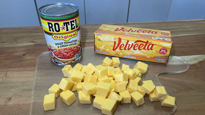A can of Rotel Original Diced Tomatoes & Green Chilies sits on a cutting board with diced Velveeta and a Velveeta box.