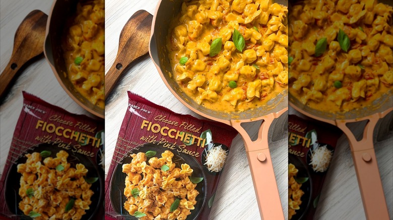 A bag of Trader Joe's Cheese Filled Fiocchetti with pink sauce sits next to a skillet full of the pasta
