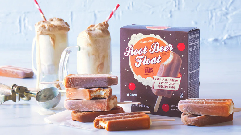 A box of Root Beer Float Bars sits next to unwrapped ice cream bars, two root beer floats in mugs, and an ice cream scoop.