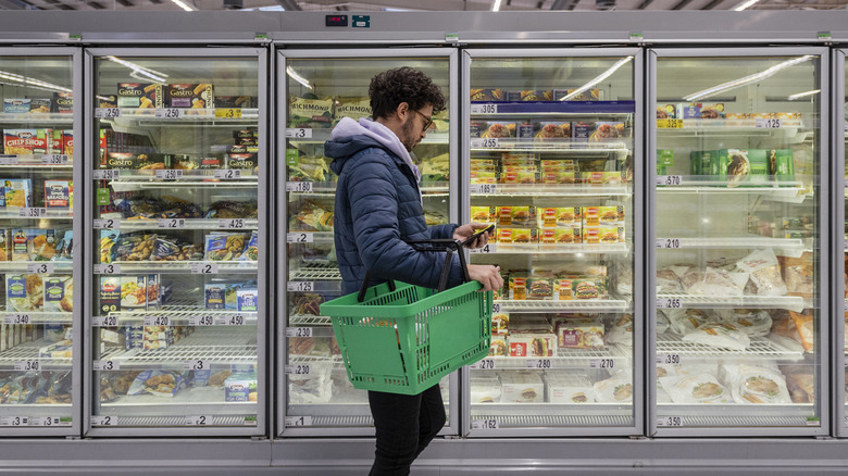 A shopper in front of a frozen food aisle in a grocery store
