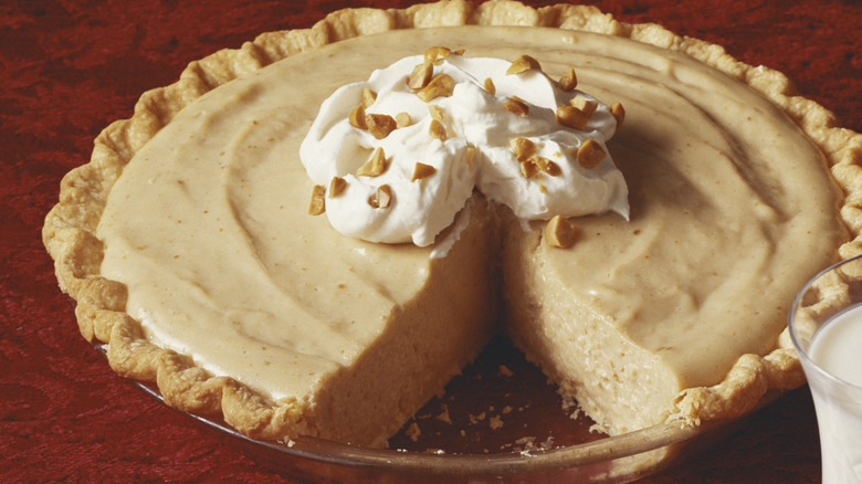 Silky peanut butter pie topped with whipped cream with one slice taken out of it