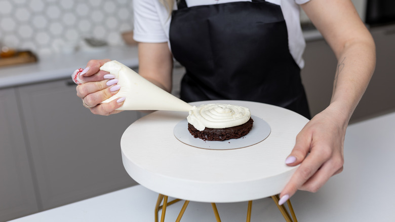 Person frosting a chocolate muffin bottom.