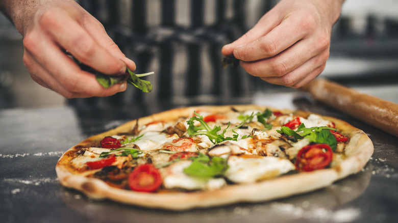 hands adding toppings to homemade pizza