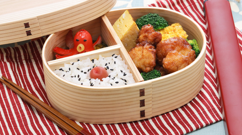 A tako sausage in a bento box on a red and white striped table mat