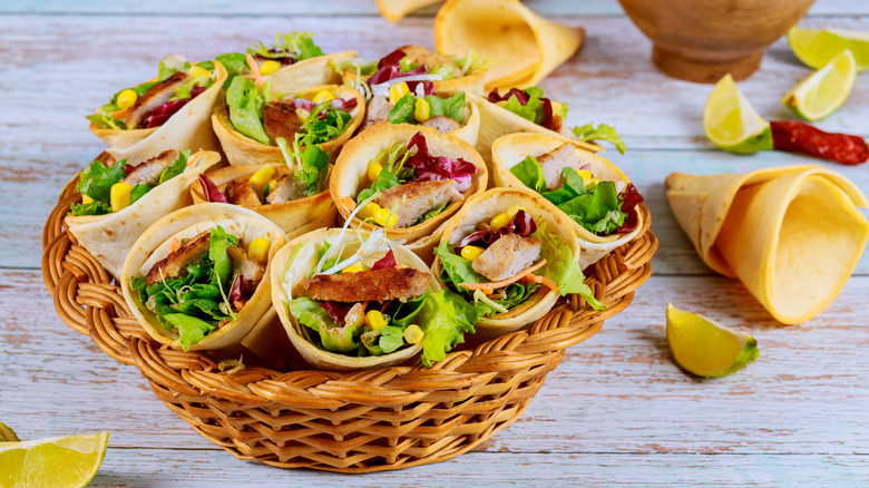 Basket with baked tortilla cones filled with grilled meat, lettuce, corn