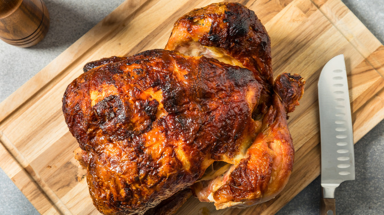 Rotisserie chicken on a wooden cutting board next to a knife.