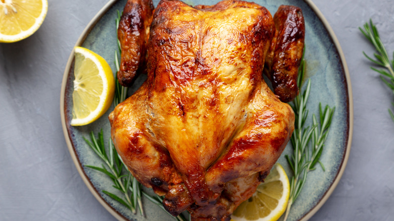 Rotisserie chicken on a plate with lemon wedges and herbs.
