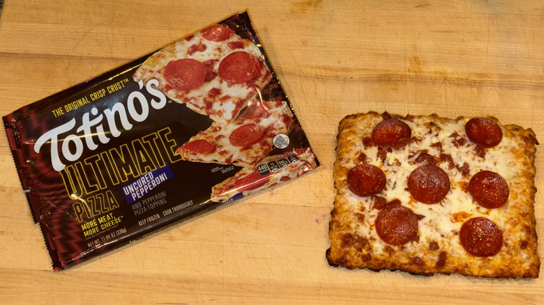 Totino's Ultimate Uncured Pepperoni Pizza baked and placed on a wooden cutting board next to the plastic wrapper