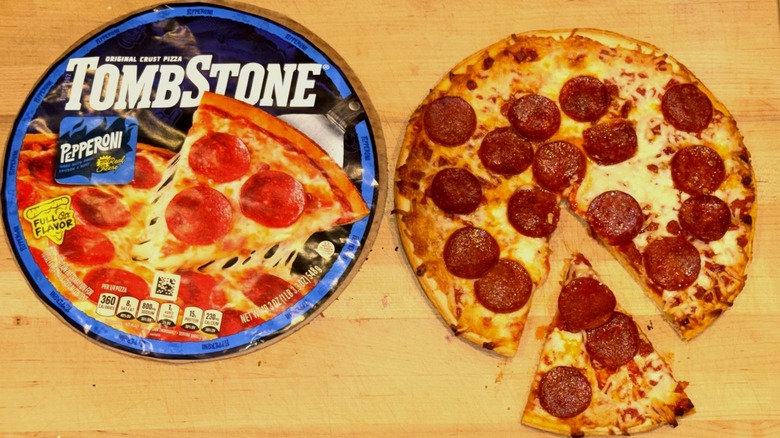 Tombstone Original Crust Pepperoni Pizza baked, with a slice cut out and pulled away, and placed on a wooden cutting board next to the box