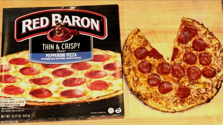 Red Baron Thin & Crispy Pepperoni Pizza baked, with a slice missing, and placed on a wooden cutting board next to the box