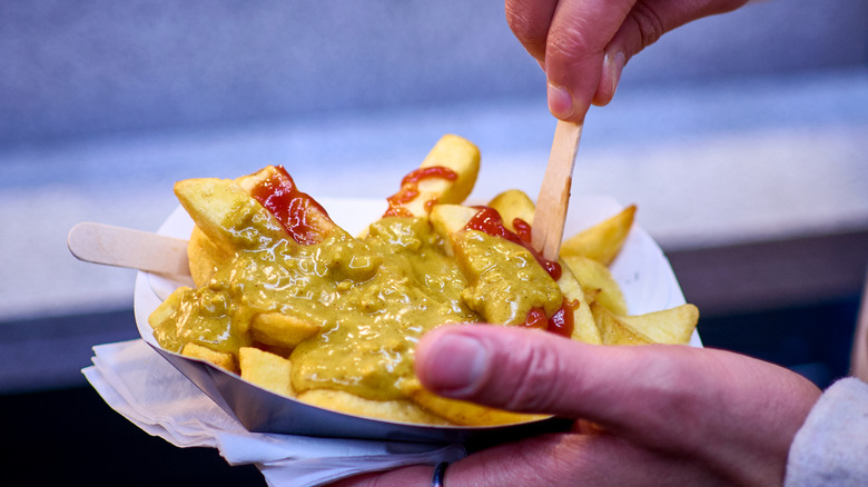 Hand holding paper bowl of fries smothered with curry