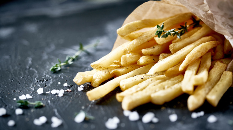 Paper sleeve of french fries with large chunks of salt