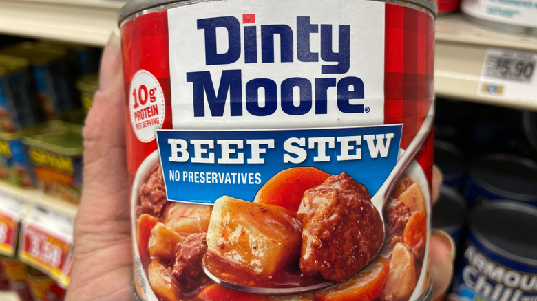 A hand holding a can of Dinty Moore Beef Stew at the grocery store.