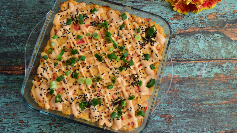 A delicious-looking, green onion-topped sushi bake sits on a faded wooden surface