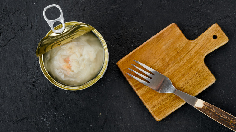 Opened can of crabbed white meat crab next to fork on black background