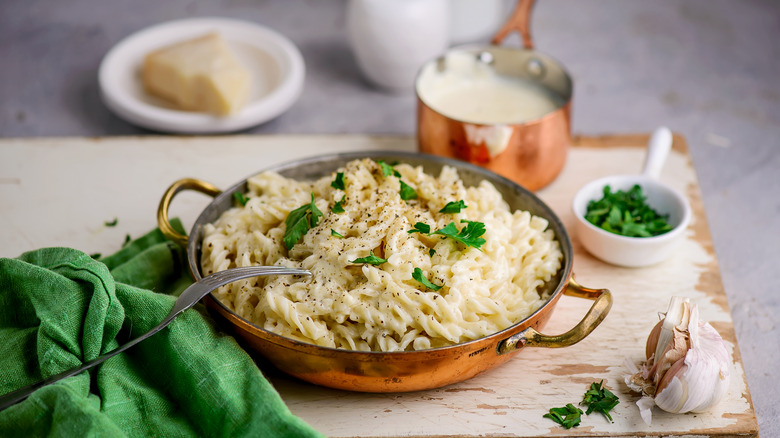 Bowl of creamy alfredo pasta with parmesan cheese, herbs, and cream in a copper pot