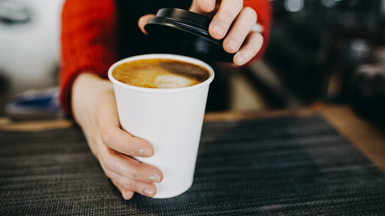 A hand holds a to-go coffee.
