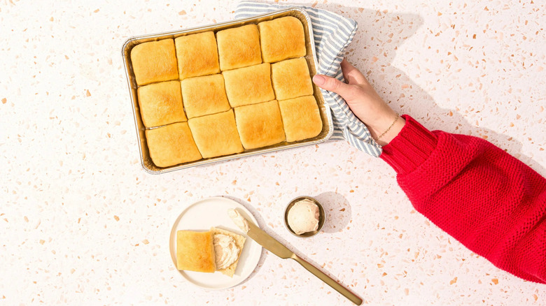 A hand holds a pan of Texas Roadhouse Mini Rolls using a potholder