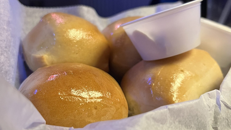 A basket of Texas Roadhouse dinner rolls with a container of Honey Cinnamon Butter