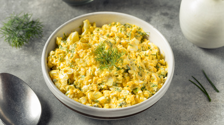 A bowl of egg salad topped with a sprig of dill