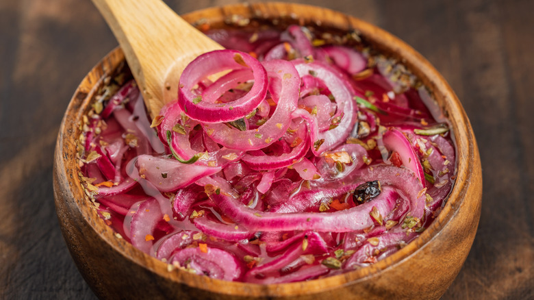 A wooden bowl filled with sliced, pickled red onions
