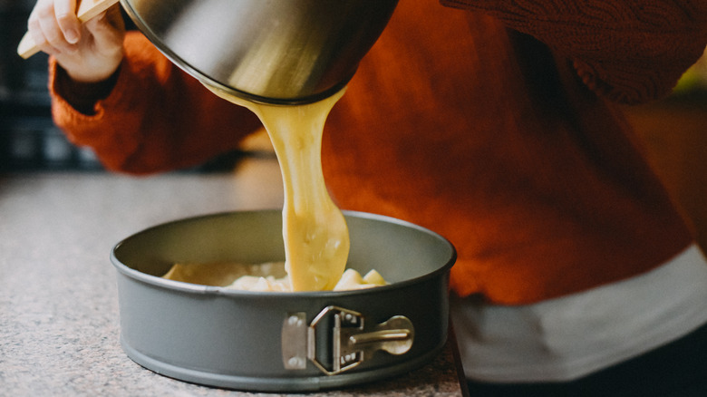 Person pouring cake mix batter into a cake pan.