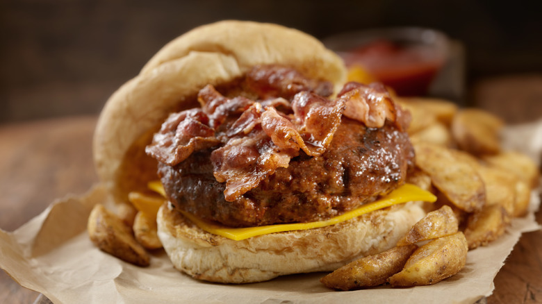 A burger topped with crispy bacon with a side of potato wedges