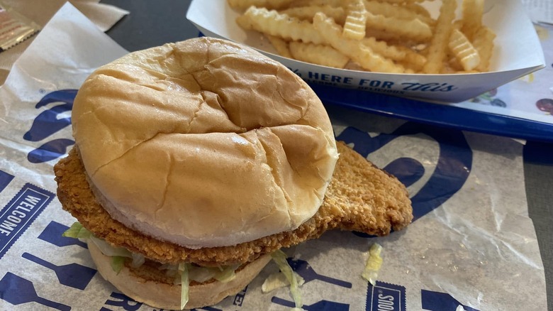 A Culver's Pork Tenderloin Sandwich sits next to a container of french fries.