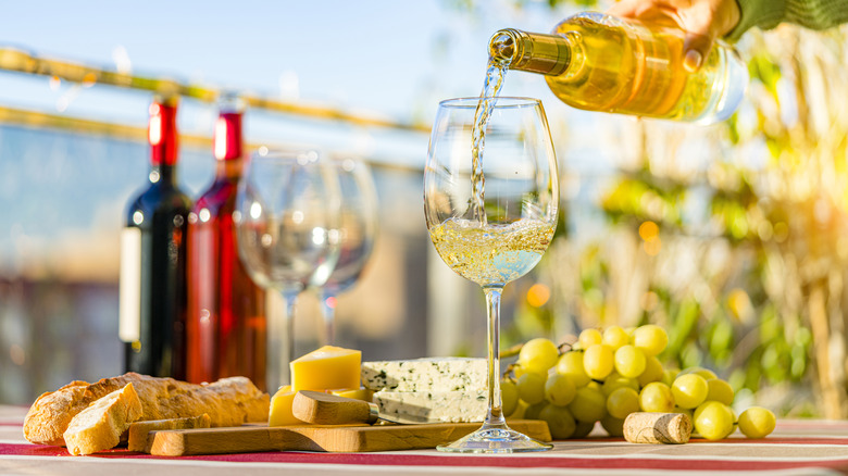 white wine being poured into a glass outdoors beside a cheese and bread plate