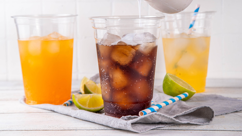 A variety of different sodas in plastic cups.