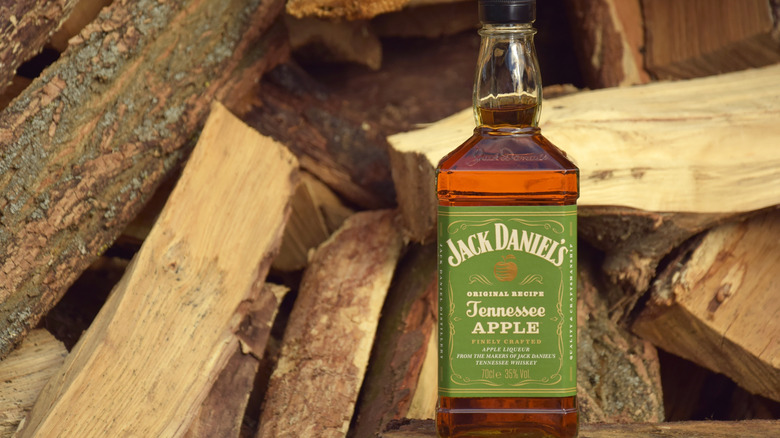 A bottle of apple flavored Jack Daniel's on logs of wood.