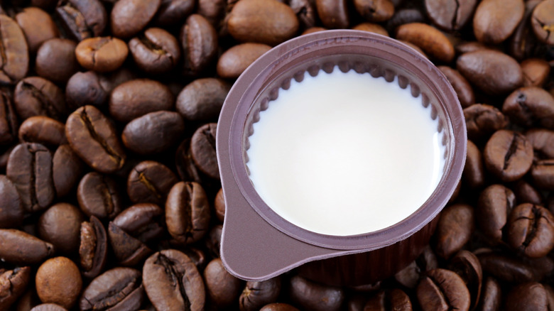 Small cup of coffee creamer on top of coffee beans background