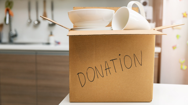 A mug and a bowl sit on top of a pile of dinnerware in a donation box.