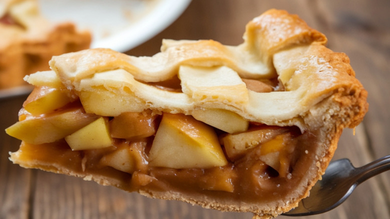 Someone holds up a slice of apple pie with a lattice pie crust