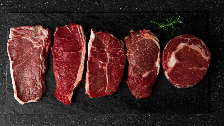 A variety of raw beef cuts on a black slab