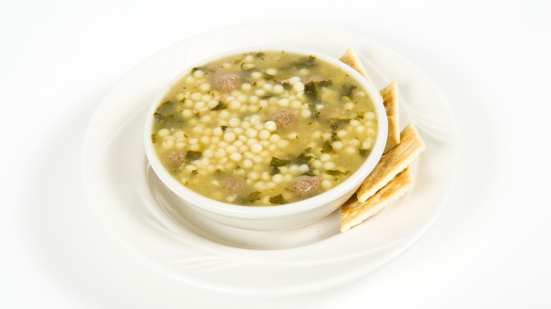 Italian wedding soup served with crackers on white background