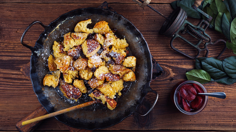 Kaiserschmarren (scrambled pancakes) sits in a dish covered with powdered sugar next to a jar of stewed cherries.