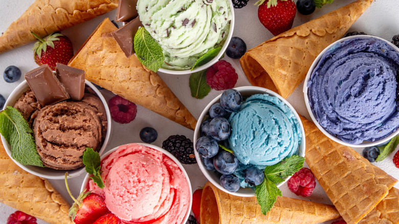 Different colored ice cream flavors in cups from above surrounded by cones