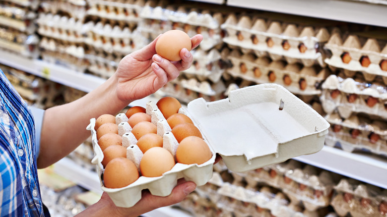 Person holding eggs in hand at supermarket.