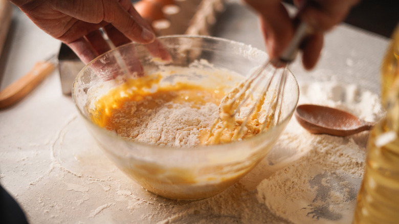 Chef whisking flour into a bowl of scrambled eggs